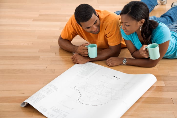 African American male and female couple lying on floor looking at architectural blueprints for their ADU