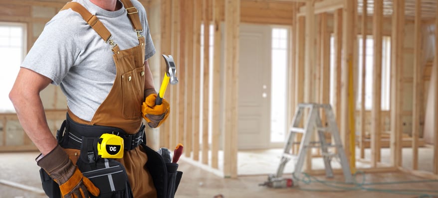 Construction owner-builder with a tool belt over new house background.