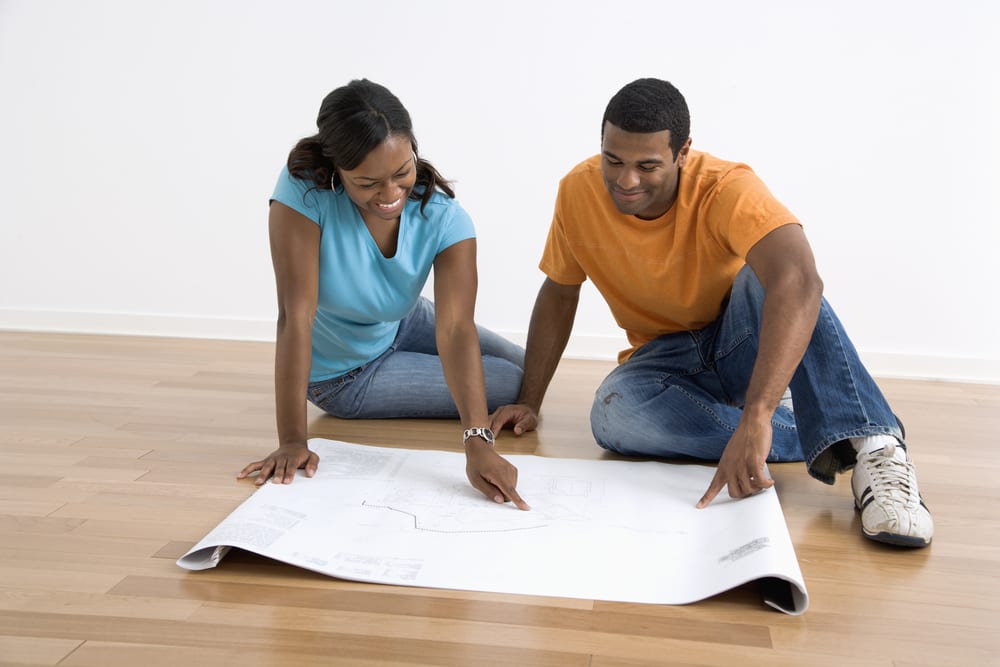 Couple sitting on floor looking at architectural blueprints.